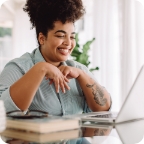 Woman sits at a desk dressed in business casual clothing and chats with someone on a laptop.